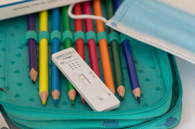 A student's colored pencils in a case, with a surgical mask and rapid covid test which is negative, on top